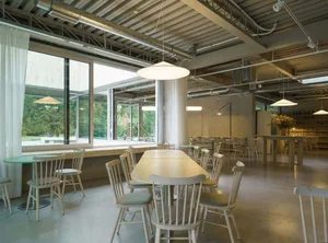 溫馨餐廳內部，設有大型木質餐桌、周圍環繞白色座椅、盆栽植物與充足座位選擇