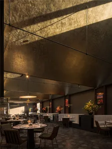 A cozy restaurant dining area with multiple tables, chairs, and potted plants, featuring wine glasses and an inviting atmosphere