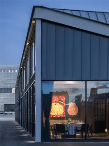 A modern dining room with a large window, curtains, two dining tables, chairs, and a decorative vase
