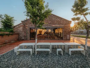 A brick restaurant building with a patio area featuring white tables and chairs, umbrellas, and a welcoming atmosphere