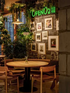 A restaurant with wooden tables and chairs, potted plants, and a variety of seating options, creating a welcoming atmosphere