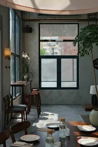 A cozy cafe with a large window, chairs, a dining table, and potted plants, perfect for enjoying a meal or coffee