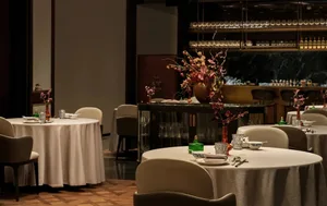 A dining area with wooden furniture, wine glasses, and vases with flowers, set in a sophisticated restaurant interior
