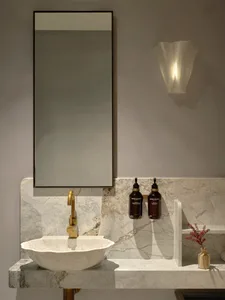 Clean modern bathroom with a marble sink, mirror, and two bottles on a countertop, surrounded by a clean and minimalist space