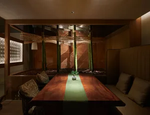 A warm and inviting Asian restaurant interior with a dining table surrounded by chairs, potted plants, and decorative vases on a green tablecloth
