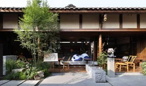 An inviting outdoor seating area with a wooden building facade, a stone table, and a large panda bear sculpture, surrounded by chairs and Asian design elements