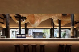 A modern bar with a unique patterned wall, stools, bottles, and wine glasses, creating an inviting atmosphere for socializing