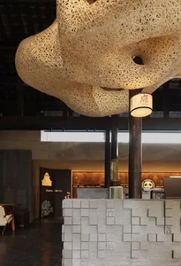 A creative interior design showroom featuring a large wooden and metal sculpture hanging from the ceiling, surrounded by smaller sculptures, furniture, and decorative pieces