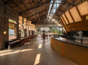 Warm and inviting open concept restaurant with wooden floors, high ceilings, and dining tables and chairs