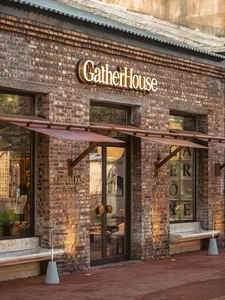 A traditional storefront with a brick exterior and a cozy interior featuring chairs and natural/artificial lighting