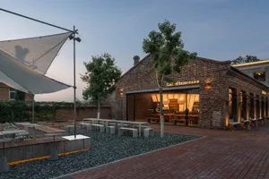A brick-floored outdoor patio with stone walls, seating areas, and dining tables, set in a pleasant environment