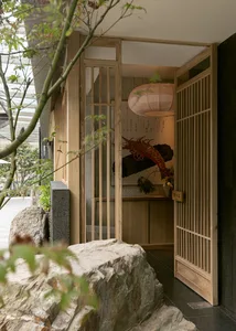 Asian-style interior design with wooden doors, stone walls, and a rock wall, featuring a potted plant and two large rocks