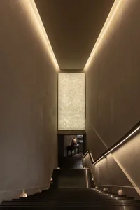 A hotel stairwell with a wooden staircase and metal railing, leading to a doorway and an inviting atmosphere