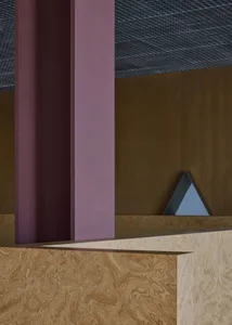 A modern commercial space with a large wooden pillar in front of a wall featuring two triangular shapes, creating a sense of depth and visual interest