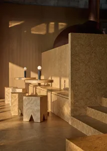 Dimly lit interior space with wooden walls and floors, featuring three small tables and chairs, and a vase on one of the tables