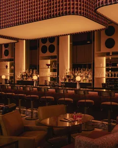 A modern bar area with a long counter and stools, featuring bottles and a stylish design