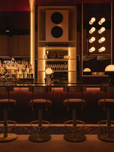 A sophisticated bar area with a long counter, stools, wine glasses, and bottles, set in a restaurant with a focus on comfort and dining experience