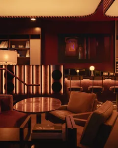 A living room with a red accent wall, multiple chairs, a dining table, a couch, a TV, and books, creating a cozy atmosphere for relaxation and reading