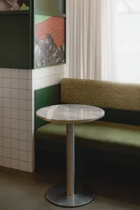 A cozy living space with a green metal bench, a dining table, and a vase, set against a neutral background