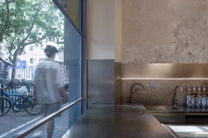 A modern kitchen with a metal countertop, a large window, and a dining table, featuring two people in the scene