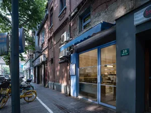 街景中帶有小型咖啡店門面、藍色遮陽篷、自行車與牆上時鐘，杯子與可能近期顧客活動