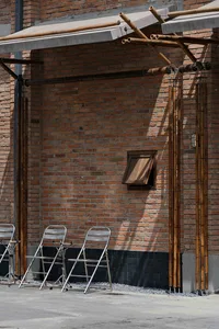 A brick building with a patio seating area featuring four chairs arranged in two rows, creating a casual and inviting atmosphere