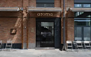 A welcoming restaurant entrance with a black doorway, glass windows, and outdoor seating area with a table and chairs