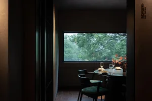 A modern dining area with a black table, chairs, wine glasses, and a vase, set in a calm and inviting atmosphere