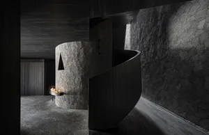 A modern living space with a stone spiral staircase, cave-like walls, a fireplace, and minimalist decor