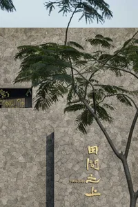 Asian-style building with stone exterior, two trees in front, and a wall with Chinese characters