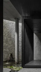 A stone hallway with two pillars on either side of the passage, leading to a doorway in a darker area of the building