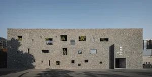 A modern building with a stone exterior, featuring multiple windows in various shapes and sizes, creating a diverse appearance