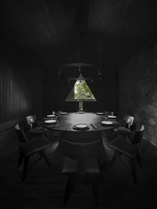 A darkened dining area with a round table and various modern chairs, creating a mysterious atmosphere