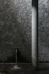 Aged stone wall with cement brick texture and two exposed pipes, one on each side, conveying a sense of history and craftsmanship