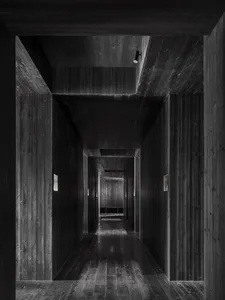 A dark and empty hallway with a wooden floor, devoid of people or objects, creating a sense of mystery