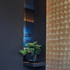 A cozy room with a dark brown wall, a gold-colored wall, a small tree in a black pot on a table, and natural light from windows