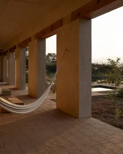 A relaxing outdoor patio with a hammock, two benches, and a chair, surrounded by natural surroundings