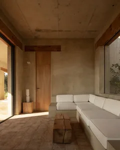 Open living area with a white couch, wooden-framed chairs, and a dining table, bathed in natural light through a window