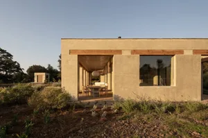 Open modern living space with natural light, wood, and concrete elements, featuring two dining tables, chairs, and a couch