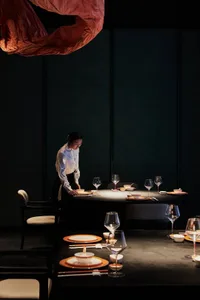 A woman stands in front of a dining table set up with wine glasses, bowls, and cups, creating an elegant and inviting atmosphere