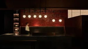 A restaurant interior with a counter and pendant lights, two people interacting with the space