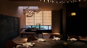 A restaurant interior with wooden floors and walls, featuring dining tables, chairs, wine glasses, and potted plants