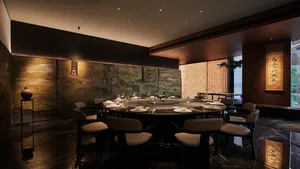 A dining table surrounded by chairs, set with plates and wine glasses, in an elegant Asian restaurant with wooden furniture