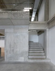 A modern staircase with concrete steps and a white wall, set in a daylight scene with possible sunlight coming through windows