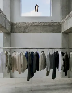 Clothing items of various styles and colors hang on a rack in front of a large window, allowing natural light to enter the space, creating a clean and well-maintained atmosphere with a focus on functionality