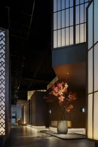 A modern lobby area with a large tree in a pot as its centerpiece surrounded by potted plants, vases, and a lively atmosphere