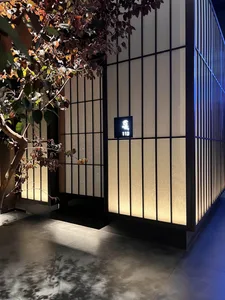 A modern Asian-style building with a wooden exterior, featuring a doorway with a sign, two potted plants, and a clock on the wall