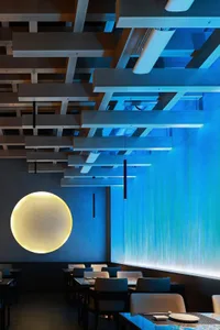 A modern restaurant dining area with a round light fixture hanging from the ceiling, illuminating the space and several chairs around the tables