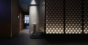 A serene hallway with a rock garden in the center, stone floor, and lights at varying heights, surrounded by Asian-style interior design elements