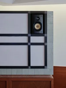 A modern wall with a grey tile design and two speakers mounted on either side, in a dimly lit room